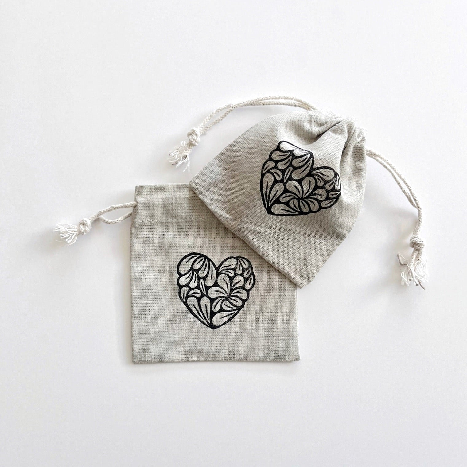 Two grey drawstring bags with black heart patterns laid on a white background