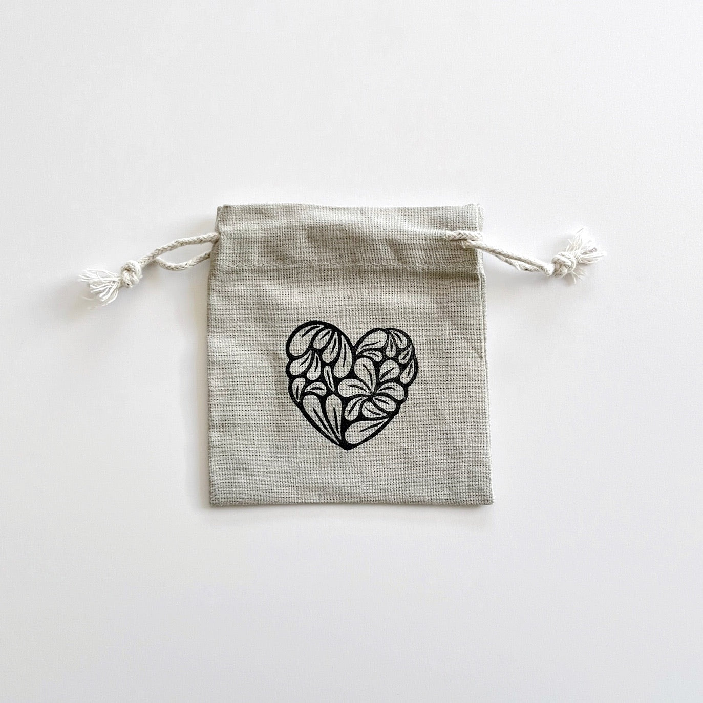 Grey drawstring bag with a black heart design laid on a white background