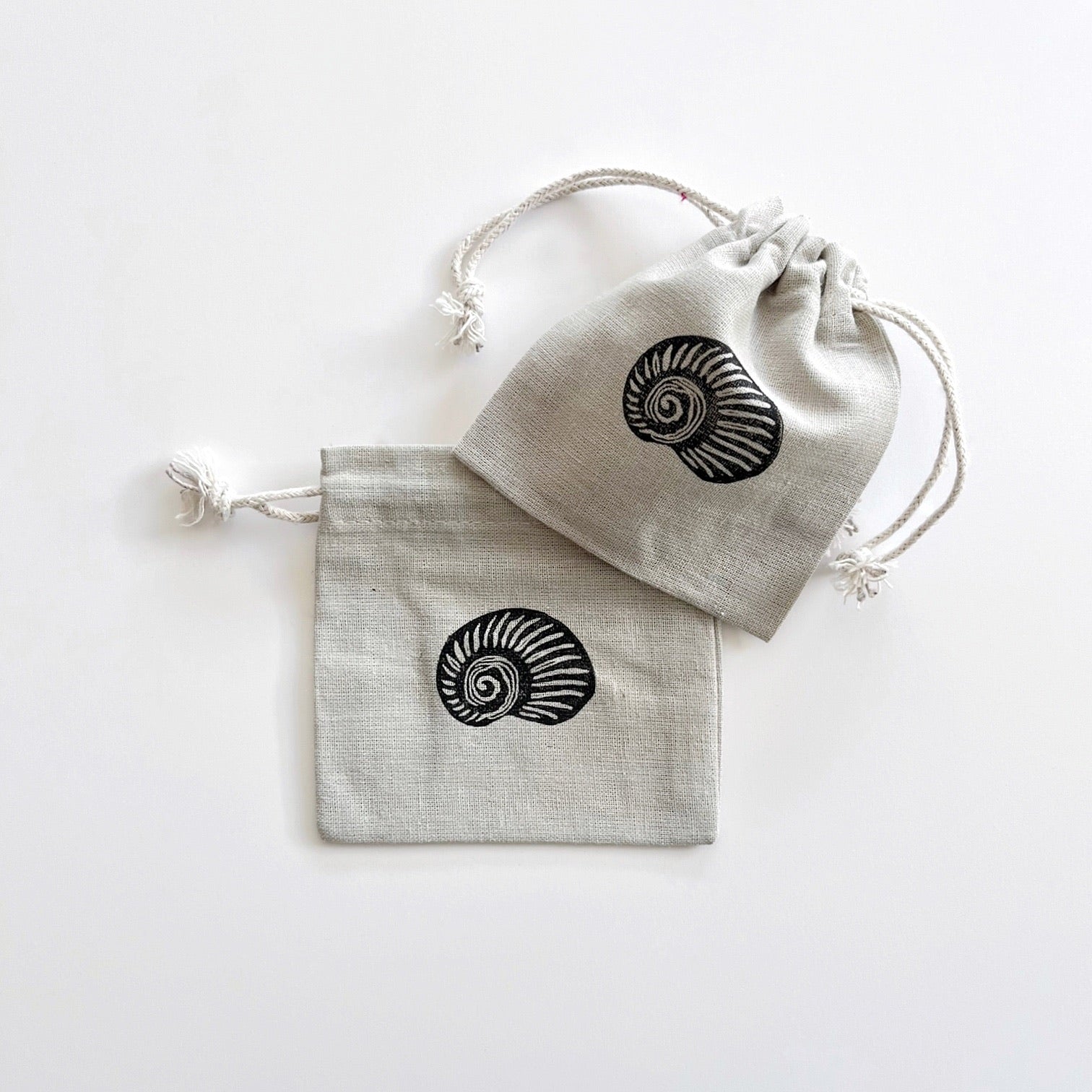 Two grey drawstring cotton gift bags with a lino printed shell, laid on a white surface.