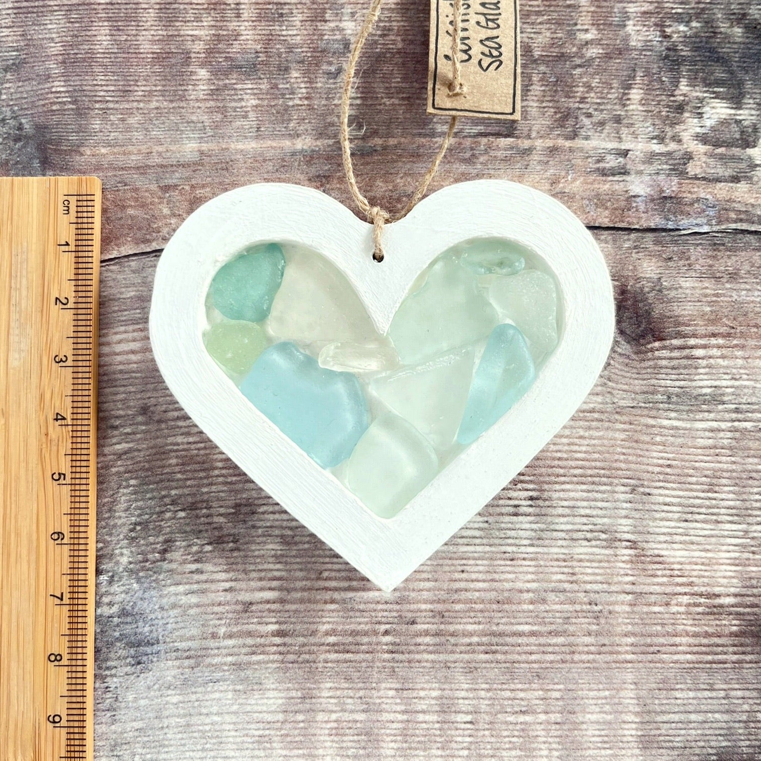 Heart-shaped sea glass hanging decoration next to ruler for scale and laid  on a wooden surface