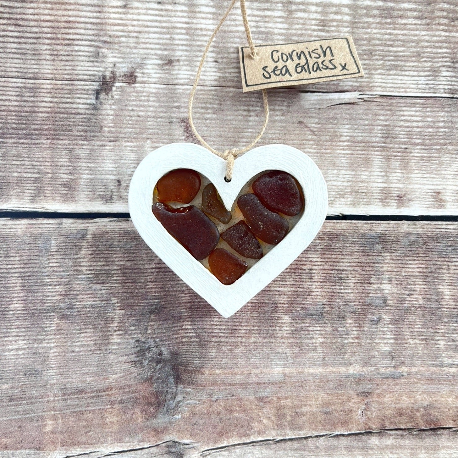 Heart-shaped sea glass hanging decoration with a 'Cornish Sea Glass' tag on a wooden surface
