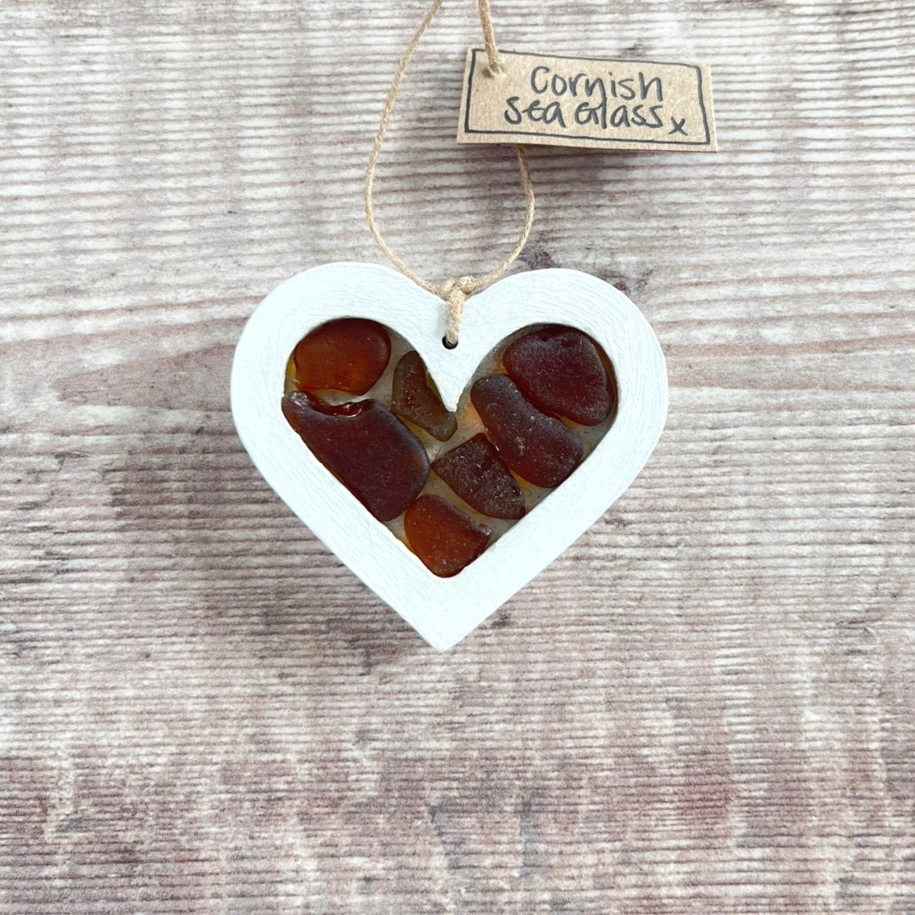 Heart-shaped sea glass hanging decoration with a 'Cornish Sea Glass' tag on a wooden surface