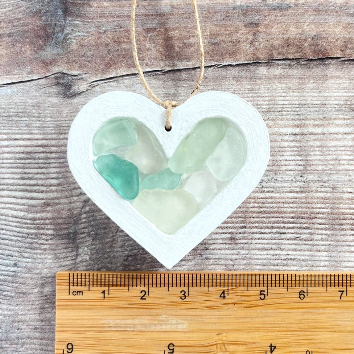 Heart-shaped sea glass hanging decoration next to a ruler for scale and laid on a wooden surface