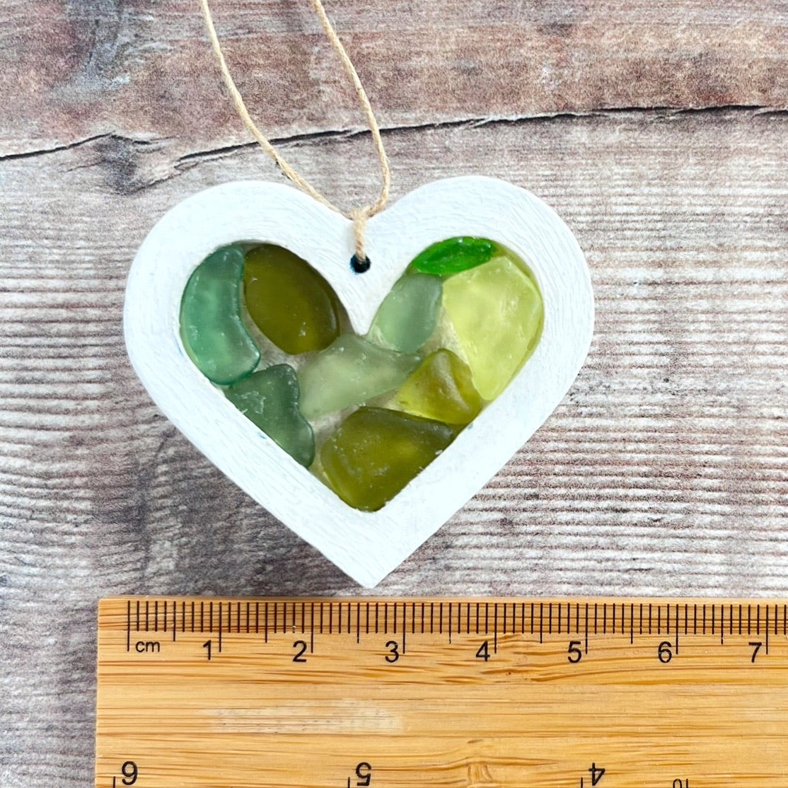 Heart-shaped sea glass hanging decoration next to a ruler for scale and laid on a wooden surface