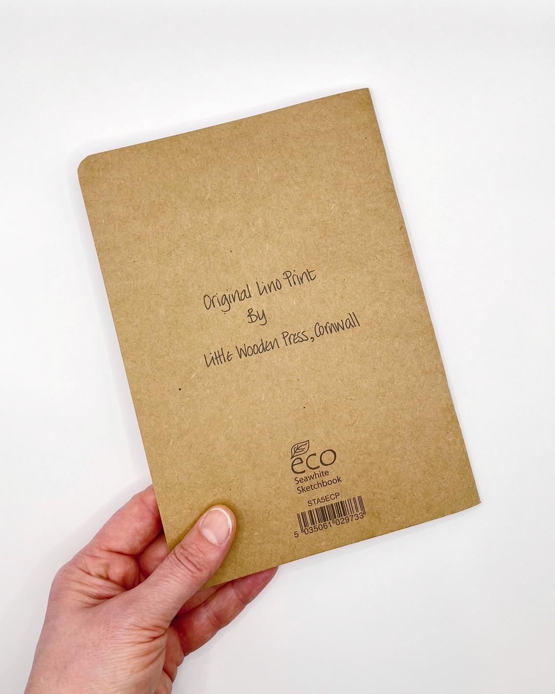 Showing the back of the Kraft sketchbook held in a hand against a white background