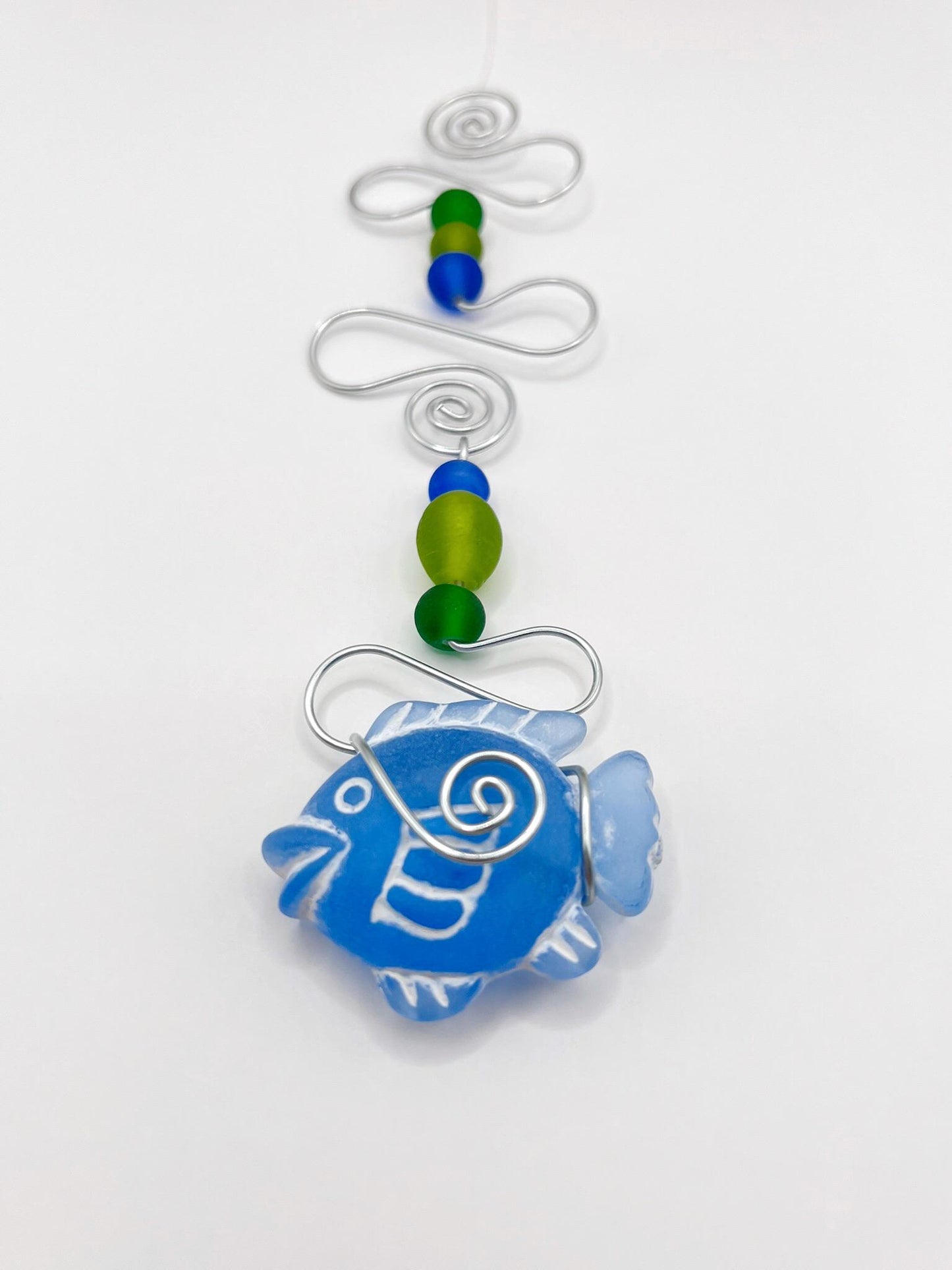 Close up of decorative hanging with blue fish, wire and coloruful beads on a white background