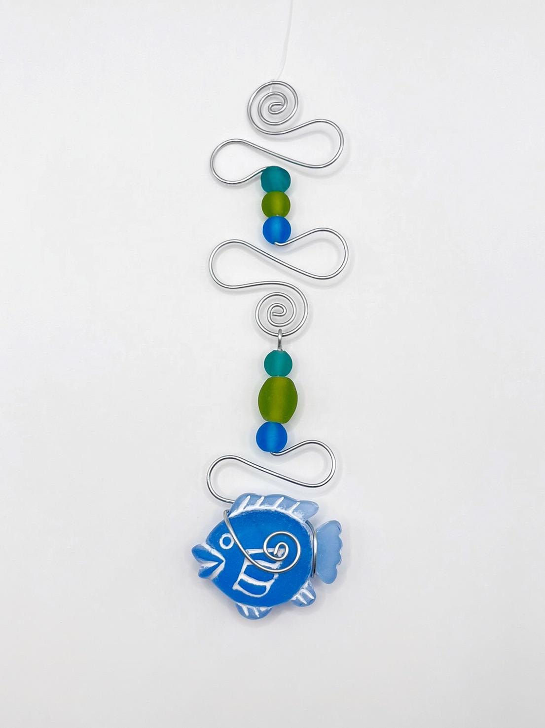 Decorative hanging ornament with blue fish, wire and colourful beads on a white background