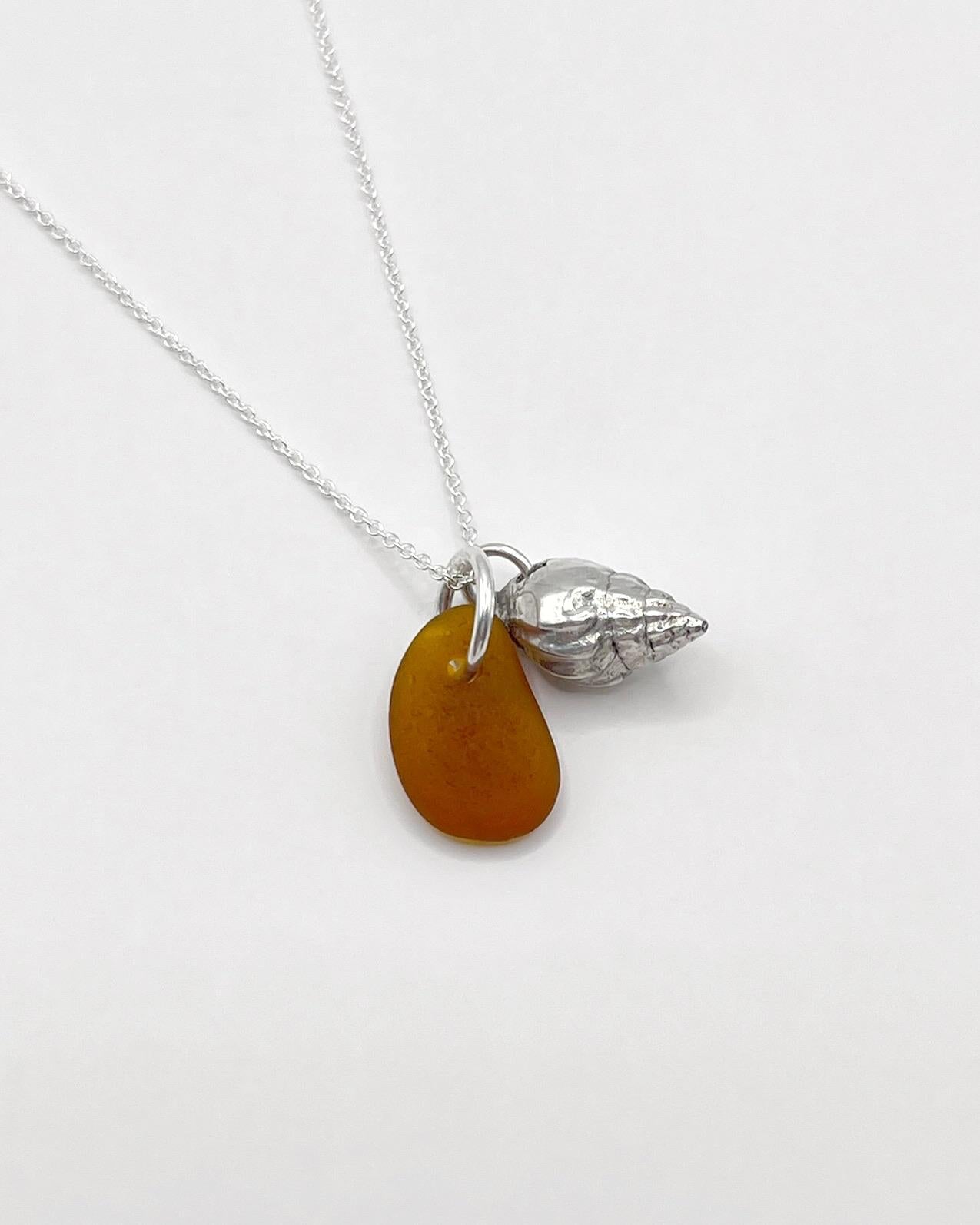 Necklace with burnt orange sea glass and silver shell pendant laid across on a white background
