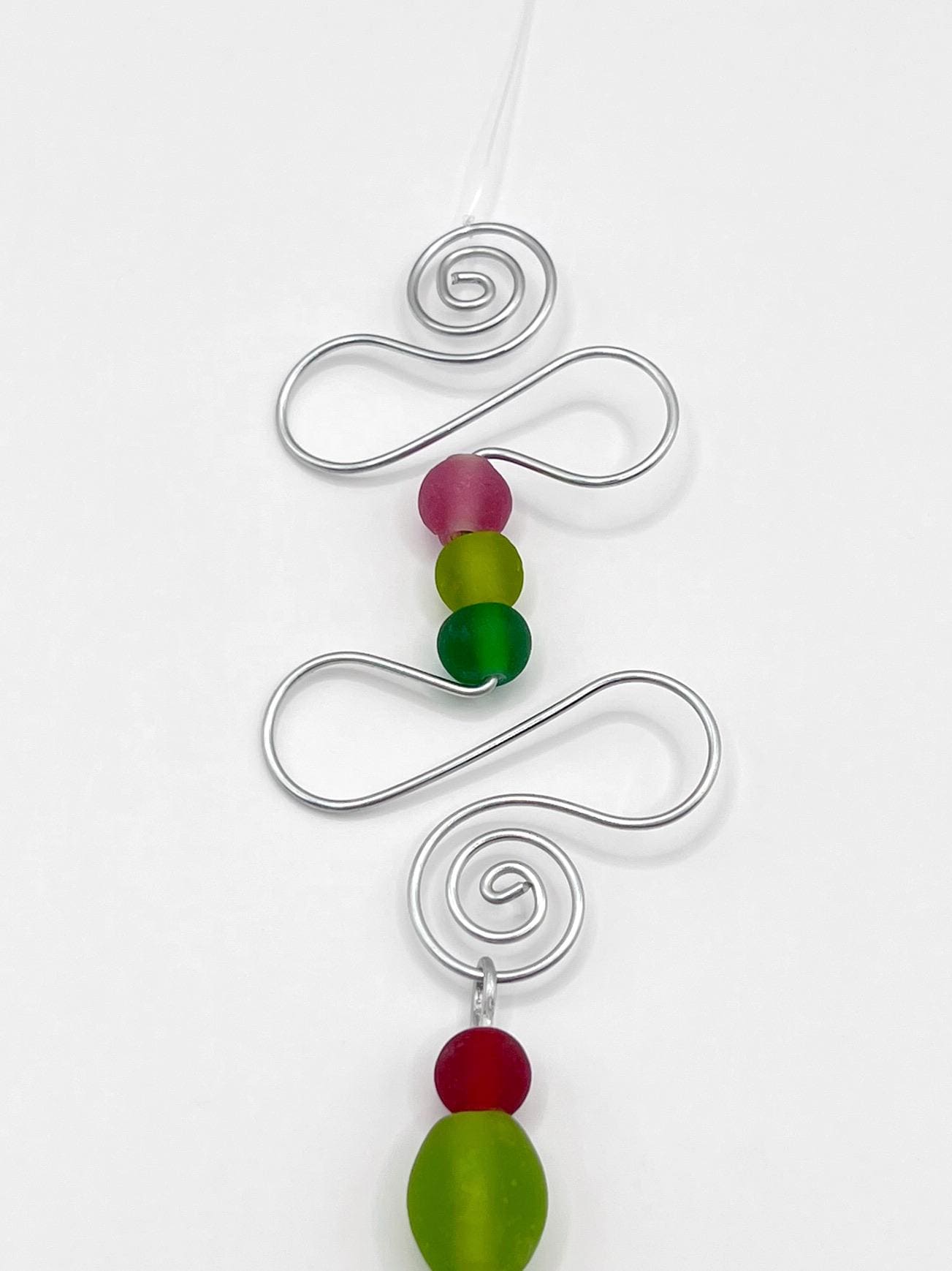 Close up of the top of decorative hanging ornament with a fish design, wire and colourful beads on a white background