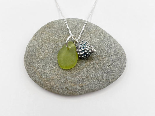 Necklace with a lime green sea glass and a silver shell charm laid on a grey pebble