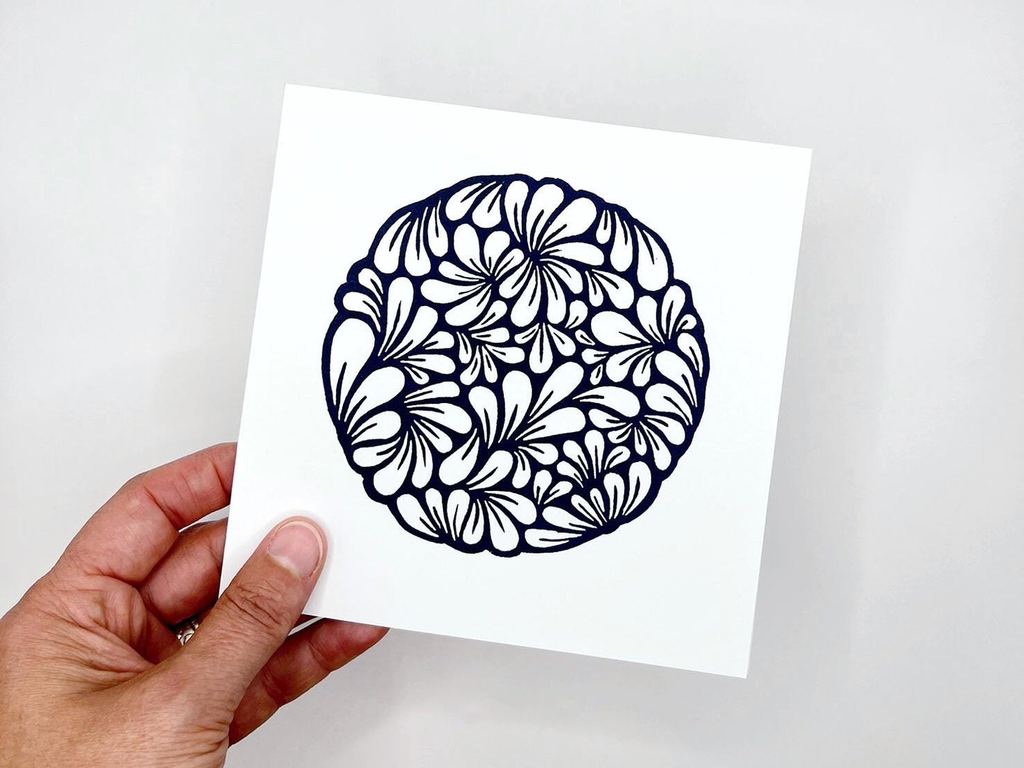 hand holding original navy blue lino printed mussel shell pattern on white card against a white background