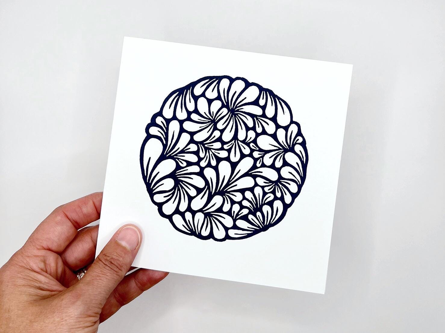 hand holding original navy blue lino printed mussel shell pattern on white card against a white background