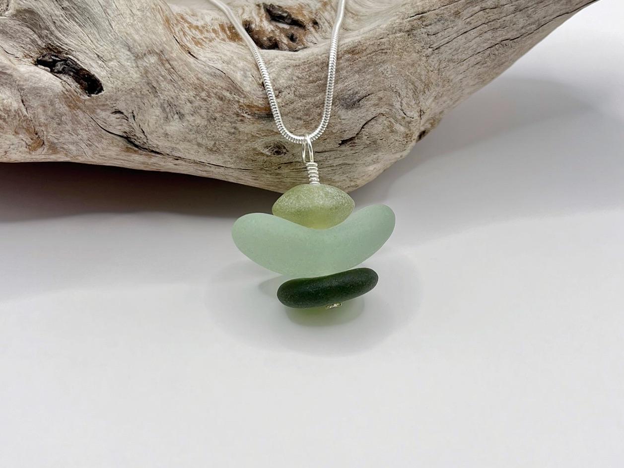 Necklace with green sea glass and Jade pendant sat against driftwood on a white background