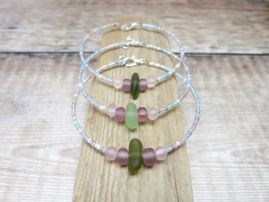 Three pastel seed beaded bracelets with green sea glass laid on a driftwood 