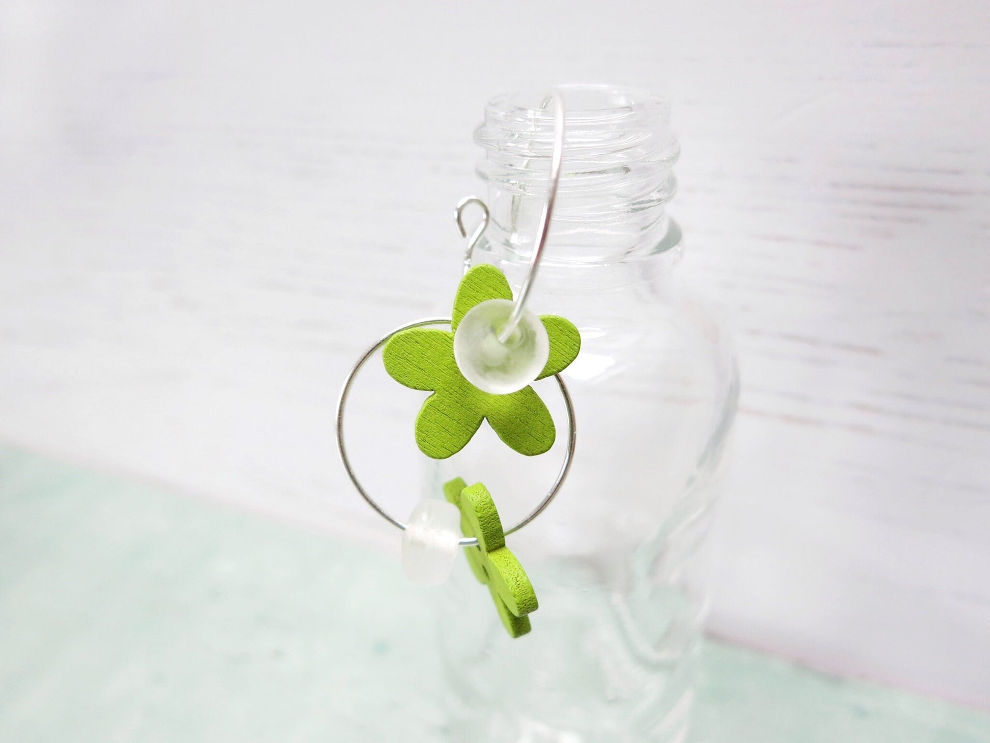 Close up of silver hoop earrings with green wooden flowers and a glass bead hung on a glass bottle