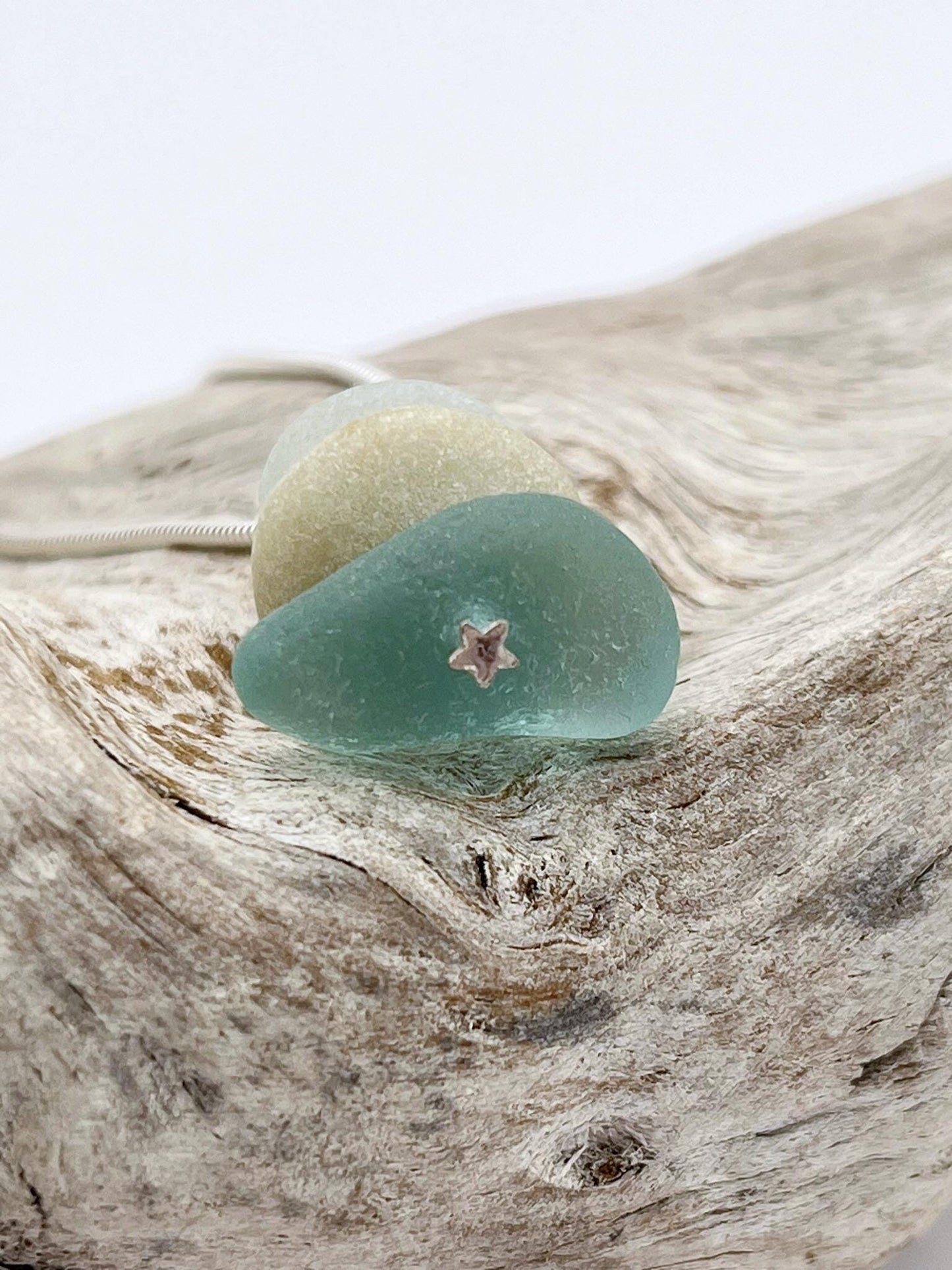 Close up of star design at the base of sea glass stack pendant laid on a piece of driftwood