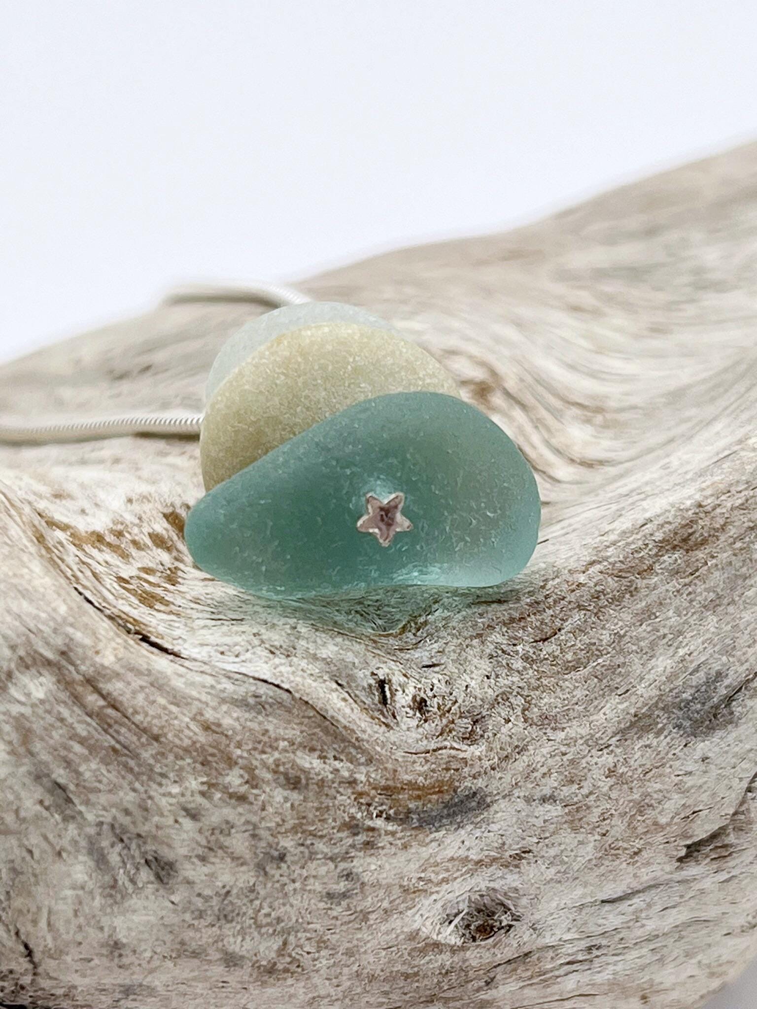 Close up of star design at the base of sea glass stack pendant laid on a piece of driftwood