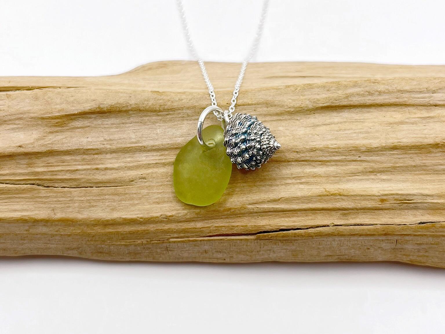 Necklace with lime green sea glass and a silver shell charm laid on driftwood