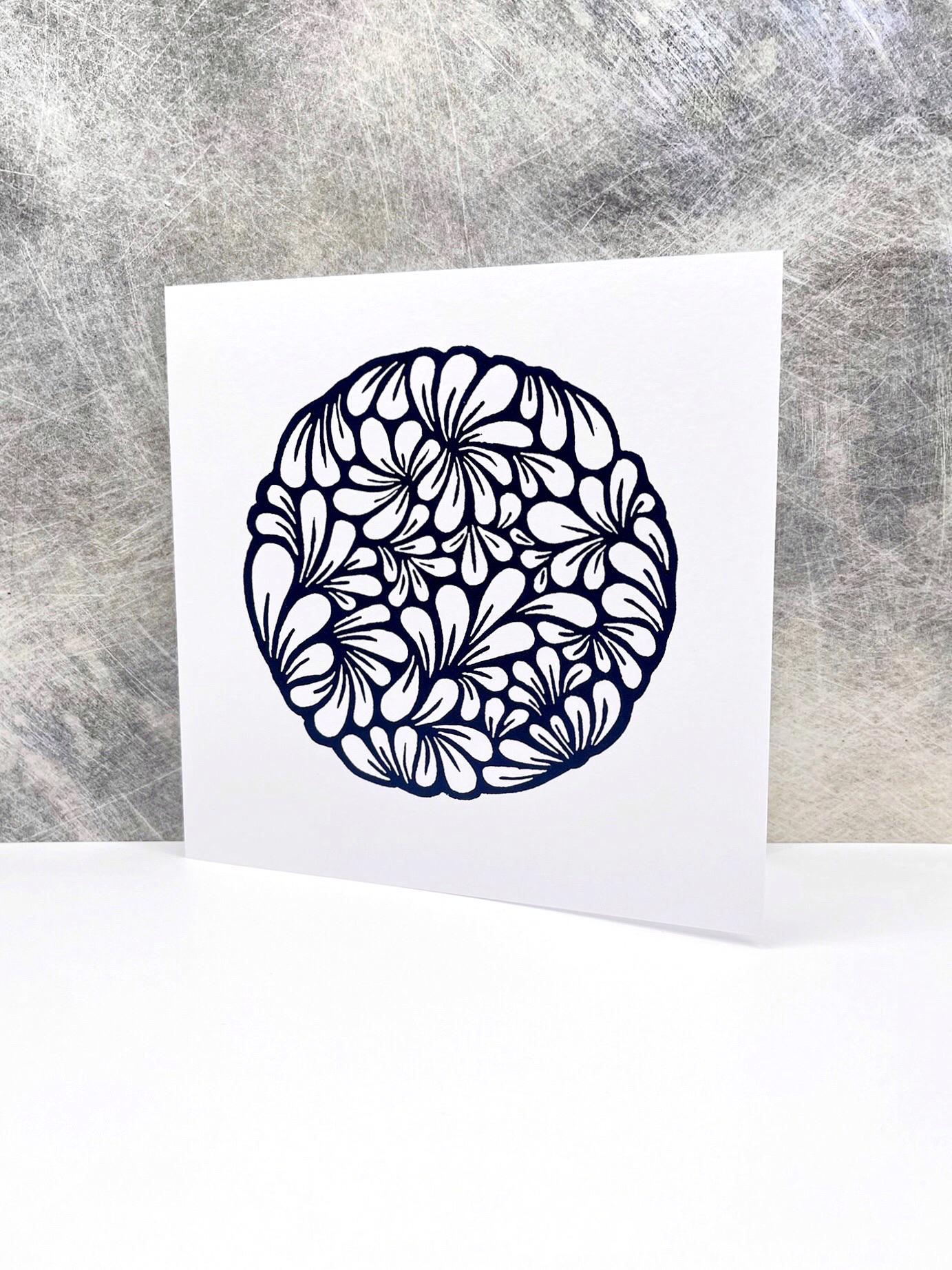 Original navy blue lino printed mussel shell pattern on white card stood against a textured background. 