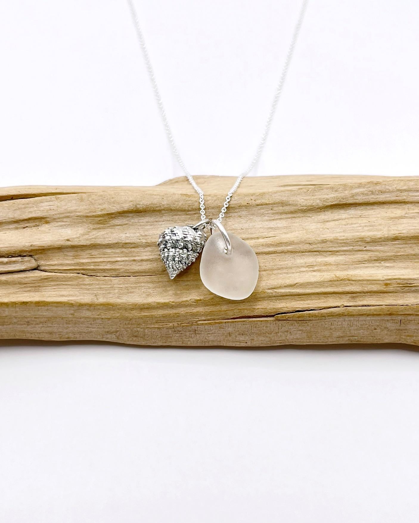 Silver necklace with White Sea glass and silver shell pendant laid on driftwood against a white background