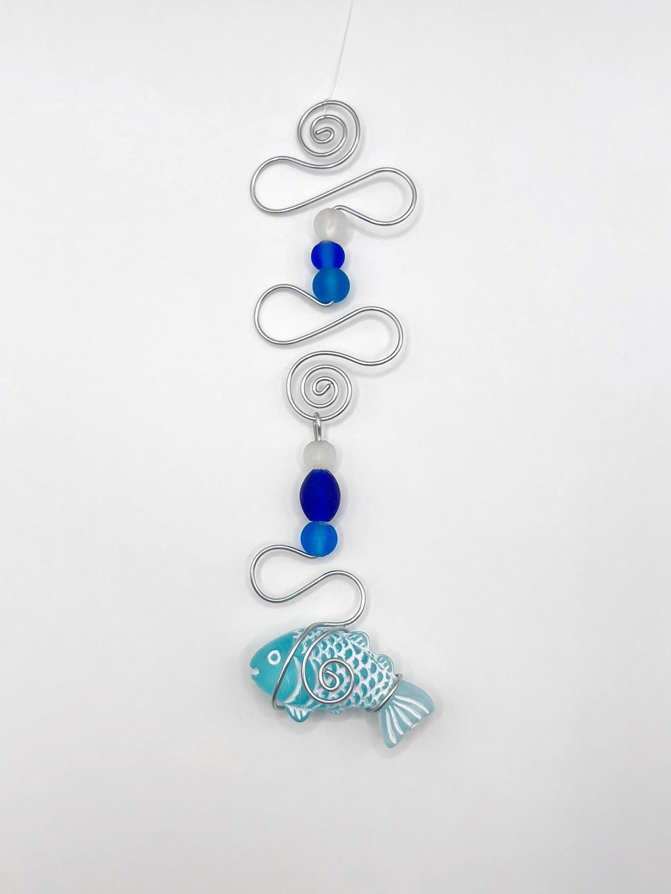 Decorative hanging fish ornament with wire and blue beads on a white background