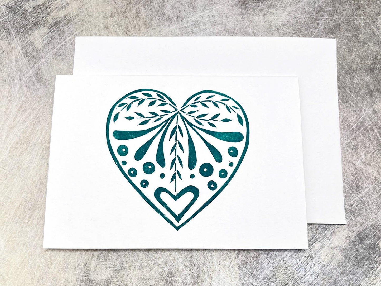 White card with an original lino printed green heart design laid on a textured surface. 