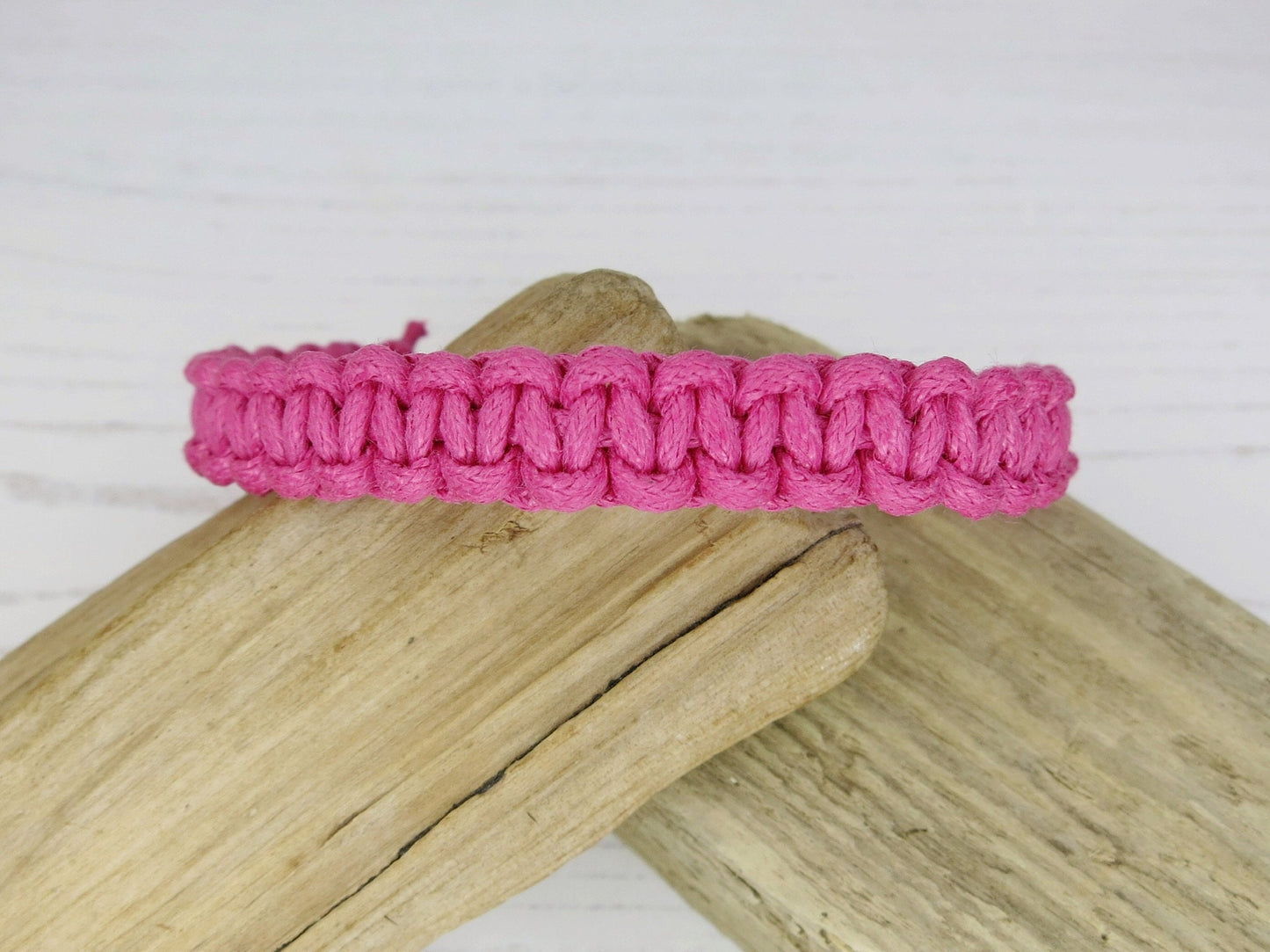 Pink macrame bracelet on a piece of driftwood with a white background