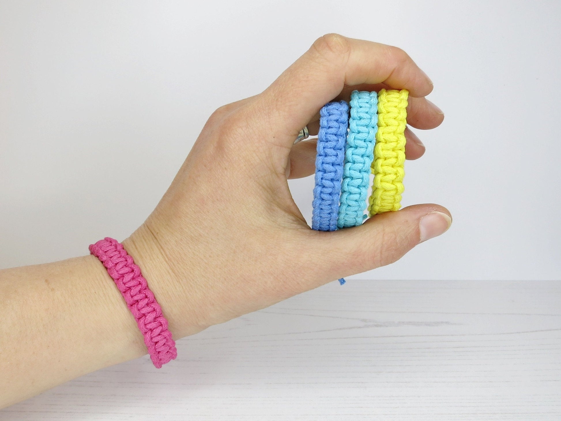Hand wearing one and holding three colorful macrame bracelets against a white background