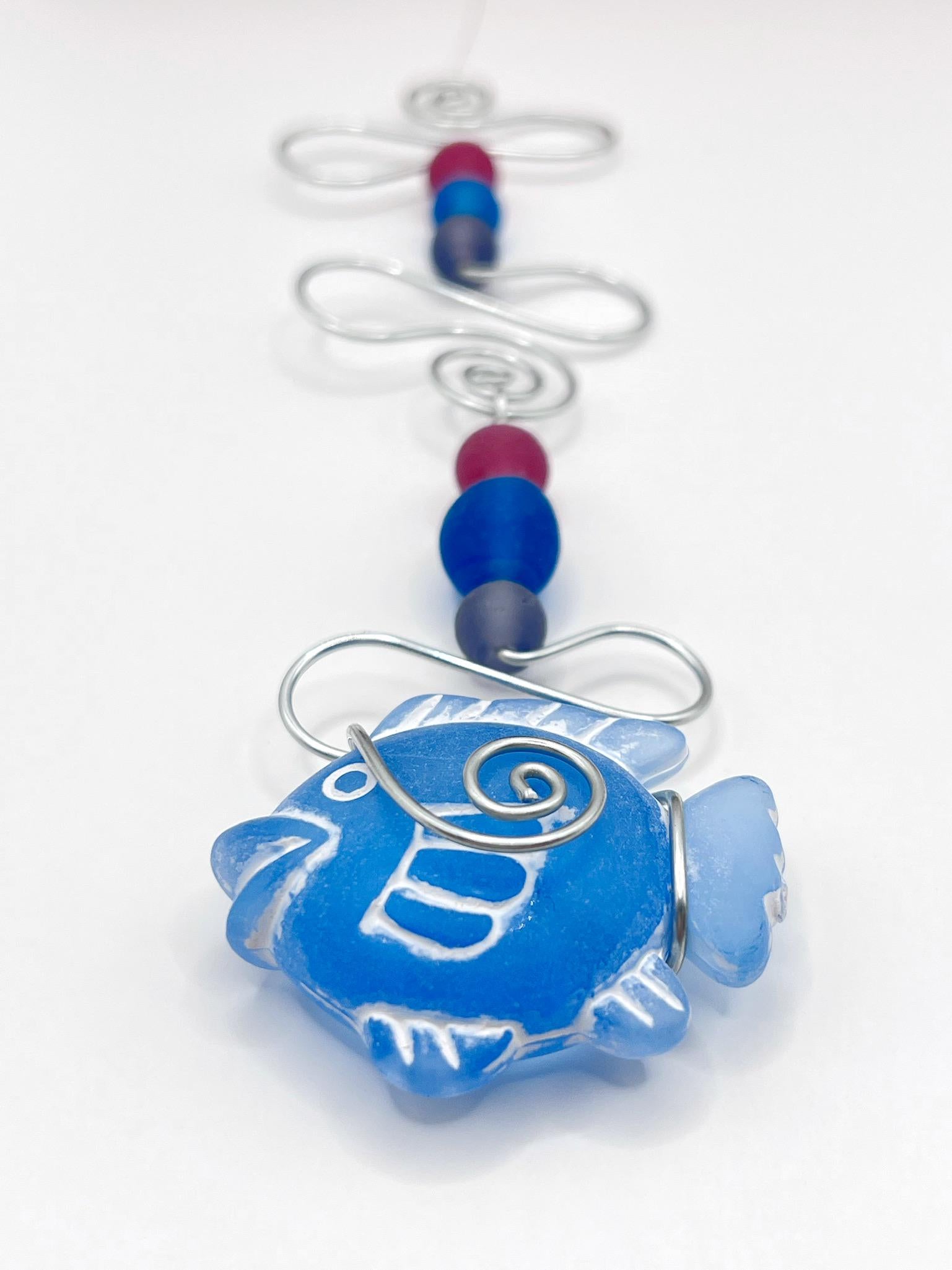 Decorative hanging ornament with blue fish design, wire and colourful beads, laid  on a white background