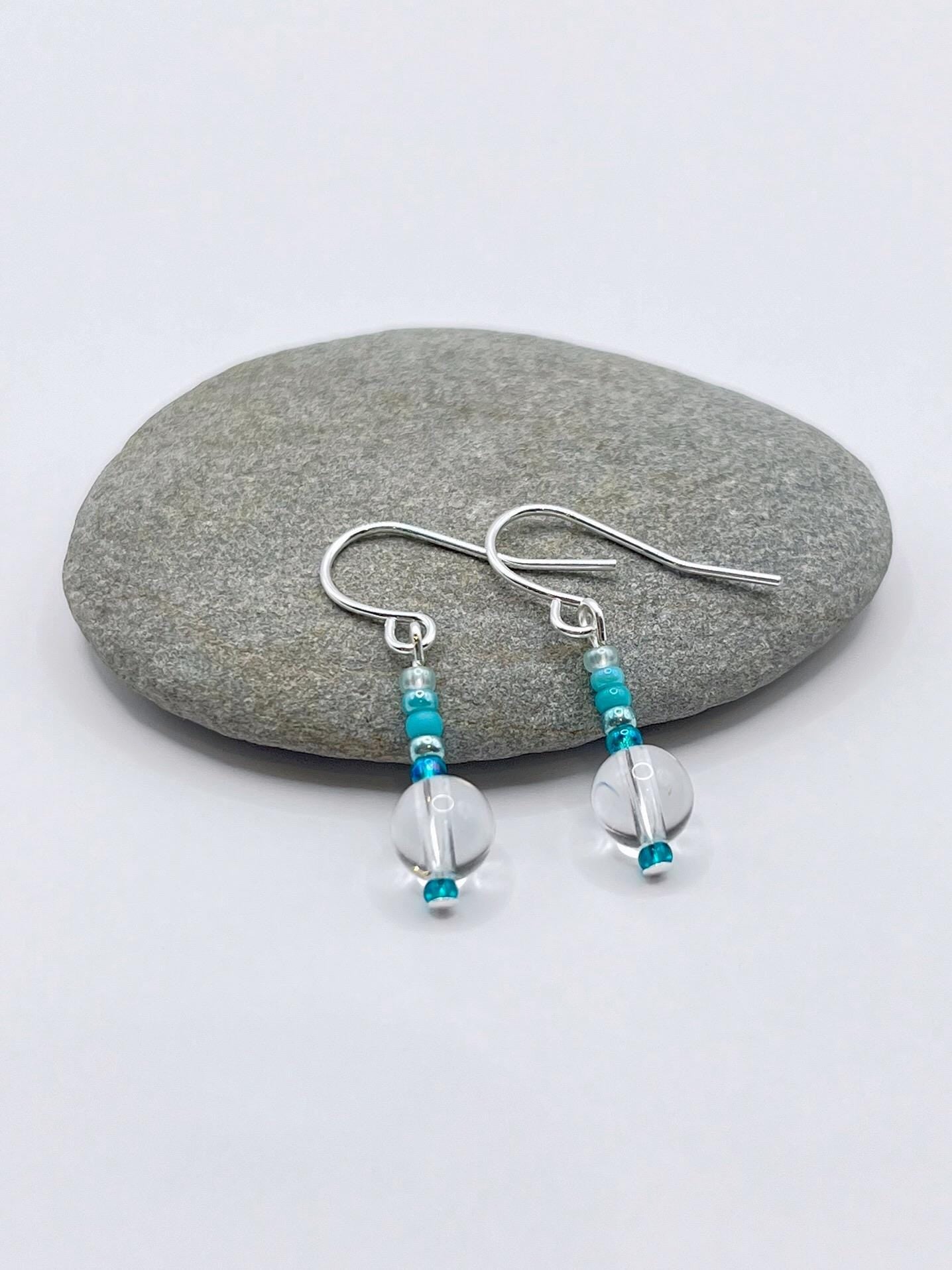 Pair of earrings with turquoise and clear crystal beads laid on a grey pebble.