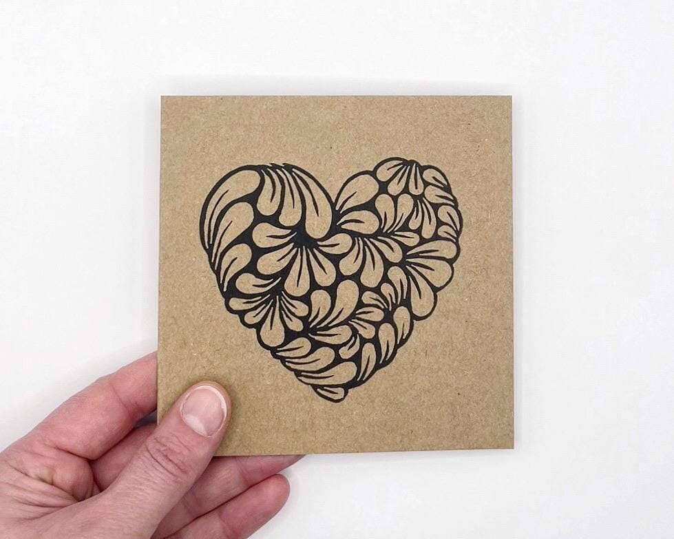 Hand holding a brown card with a black heart design against a white background