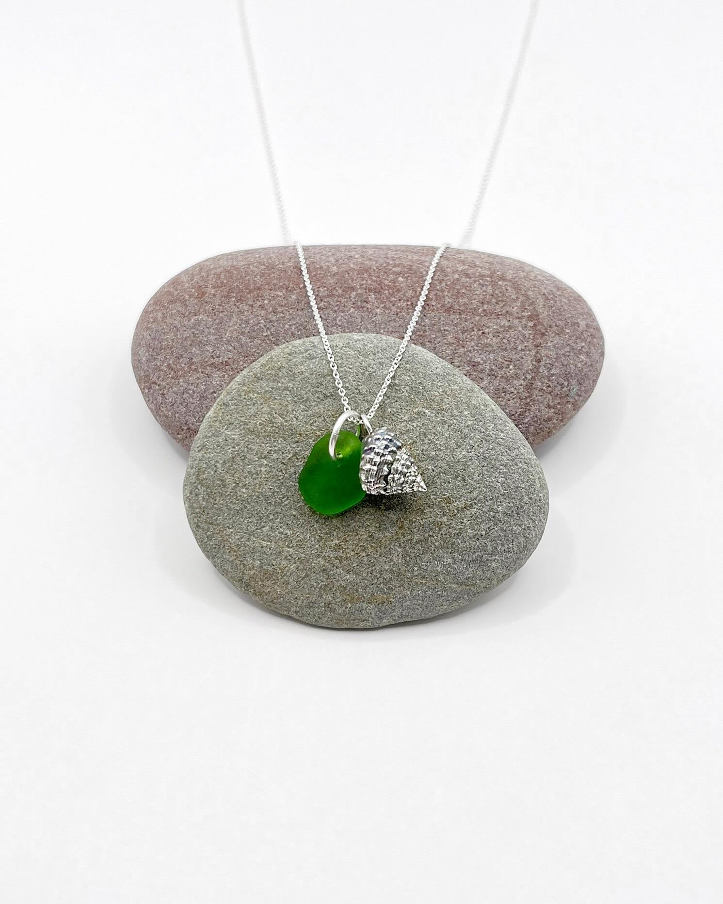 Necklace with green sea glass and silver shell pendant laid across two pebbles against a white background