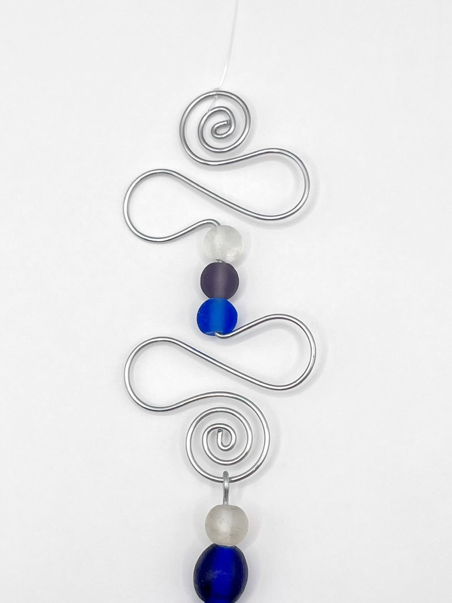 Close up of decorative hanging ornament with blue fish design, wire and glass beads on a white background