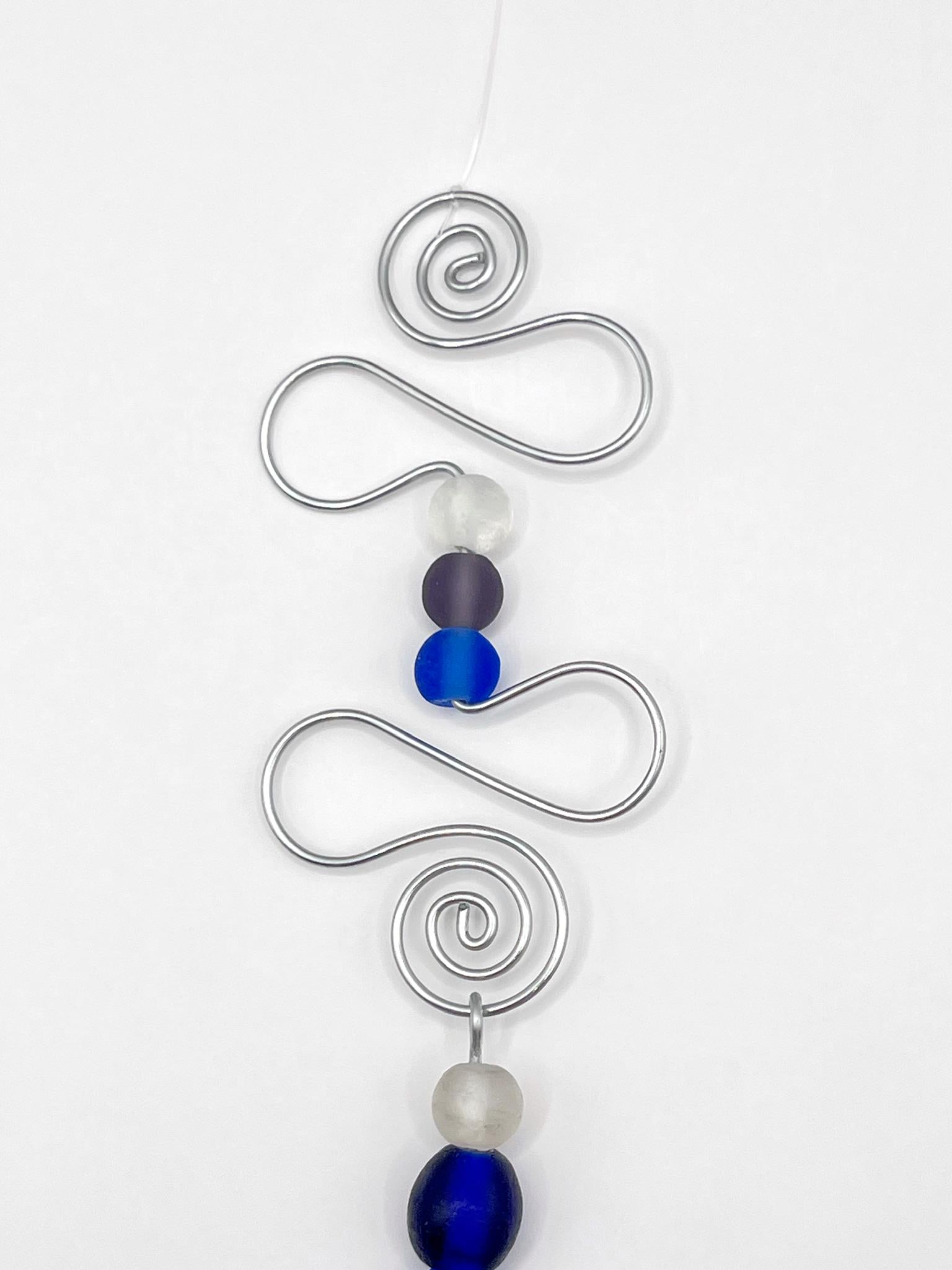 Close up of decorative hanging ornament with blue fish design, wire and glass beads on a white background