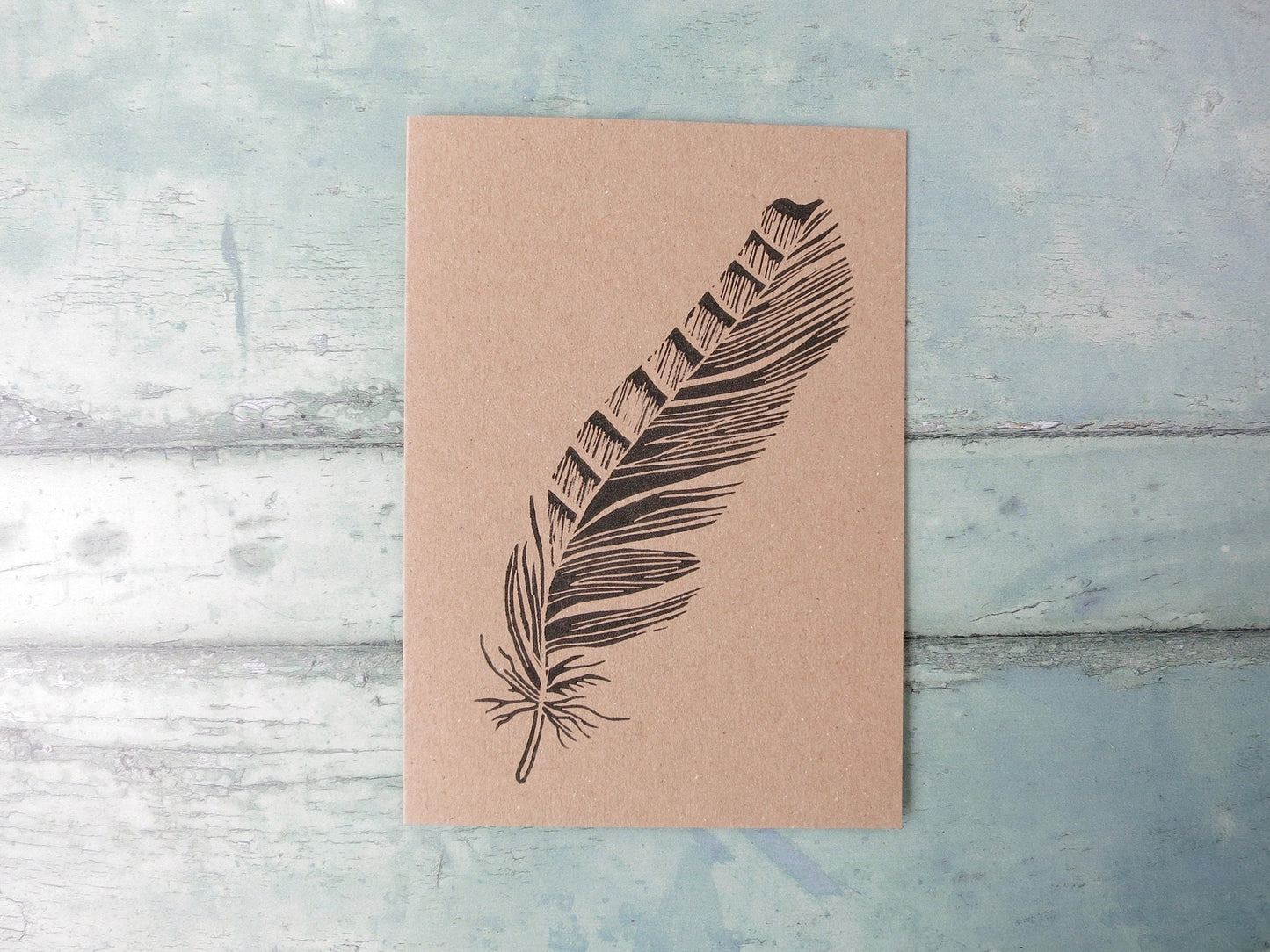 Kraft paper card with an original lino print feather laid on a textured blue surface