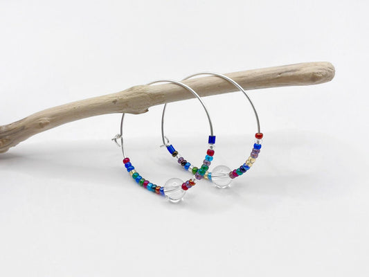 Colourful beaded hoop earrings on a white background hanging on a piece of driftwood.