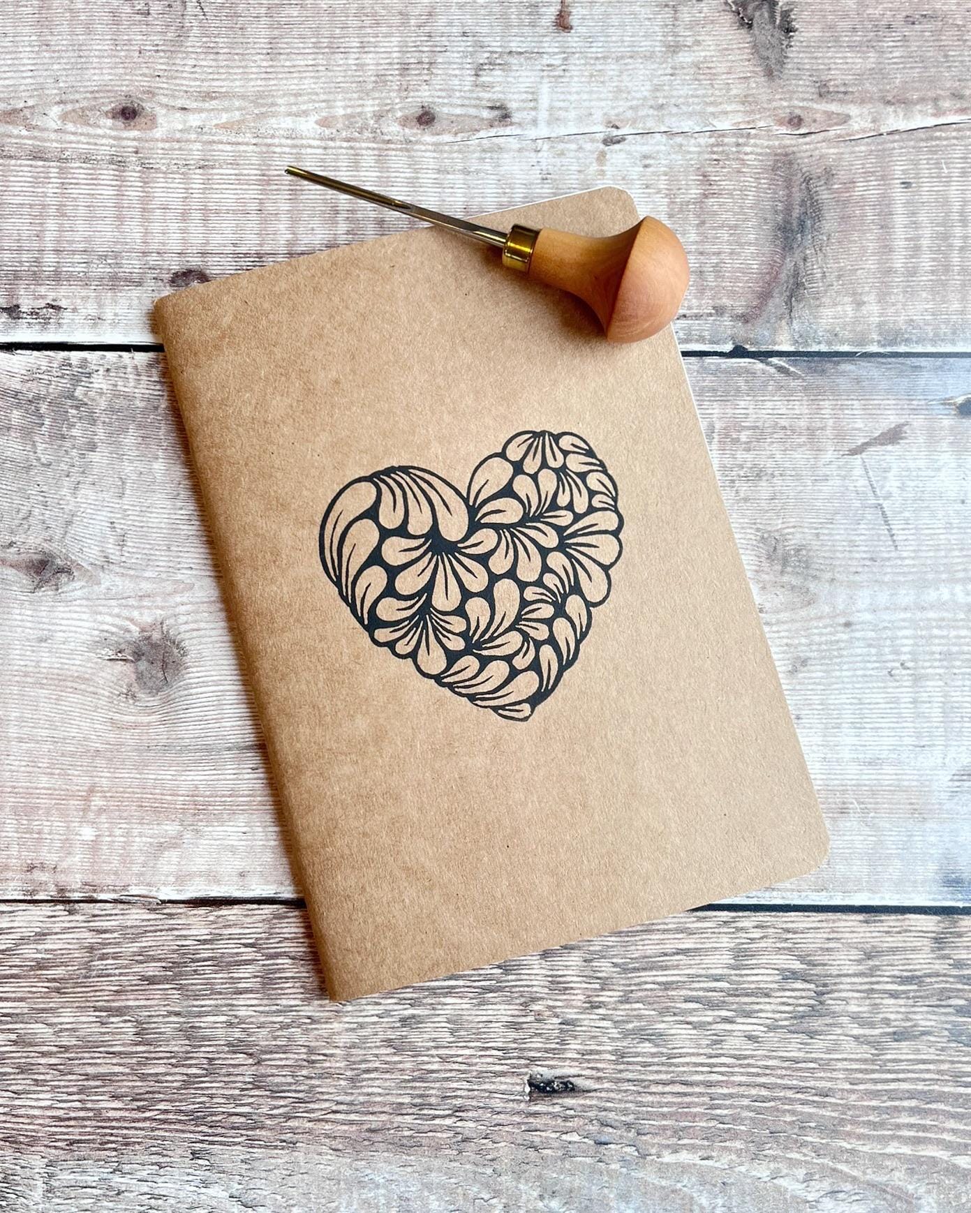 Kraft paper notebook with an original lino printed heart laid on a wooden surface