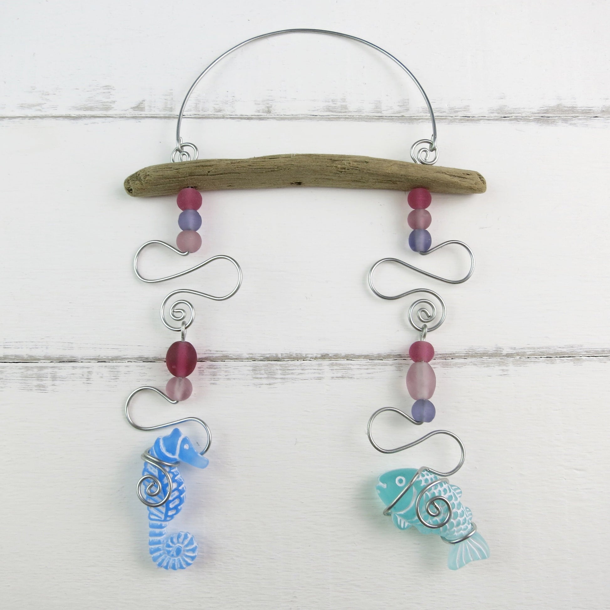 Decorative hanging mobile with a seahorse, fish, glass beads, driftwood and wire on a white wooden background