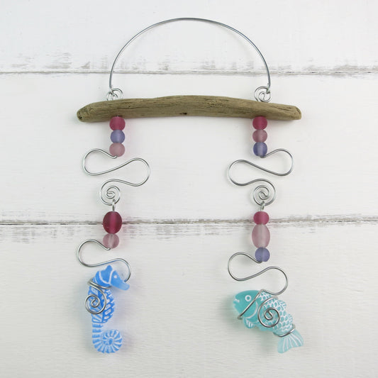 Decorative hanging mobile with a seahorse, fish, glass beads, driftwood and wire on a white wooden background