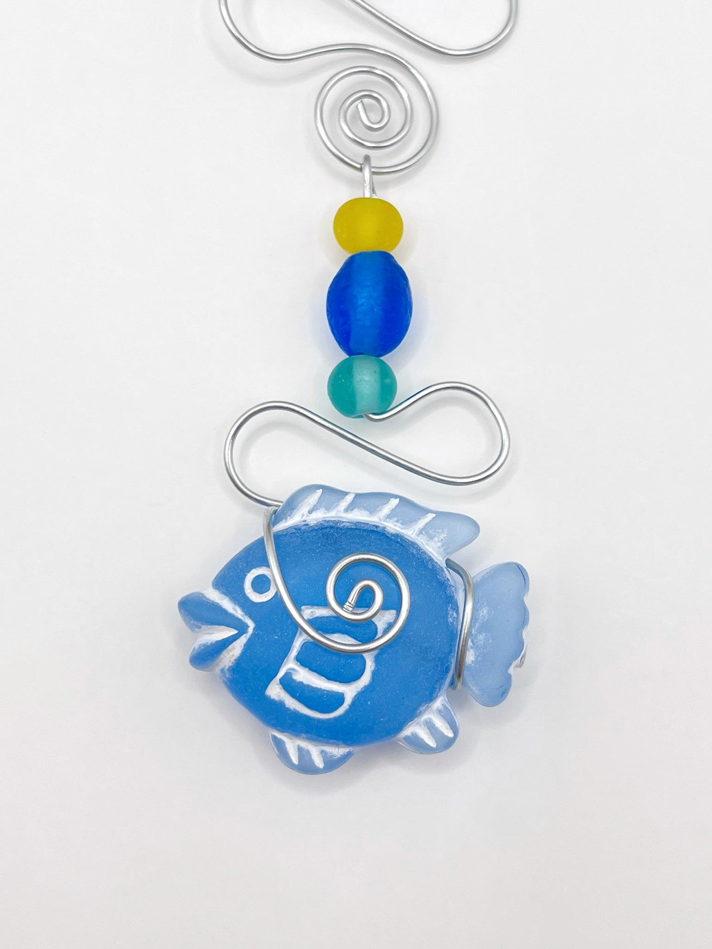 Close up of decorative ornament with blue fish design, wire and colourful beads on a white background