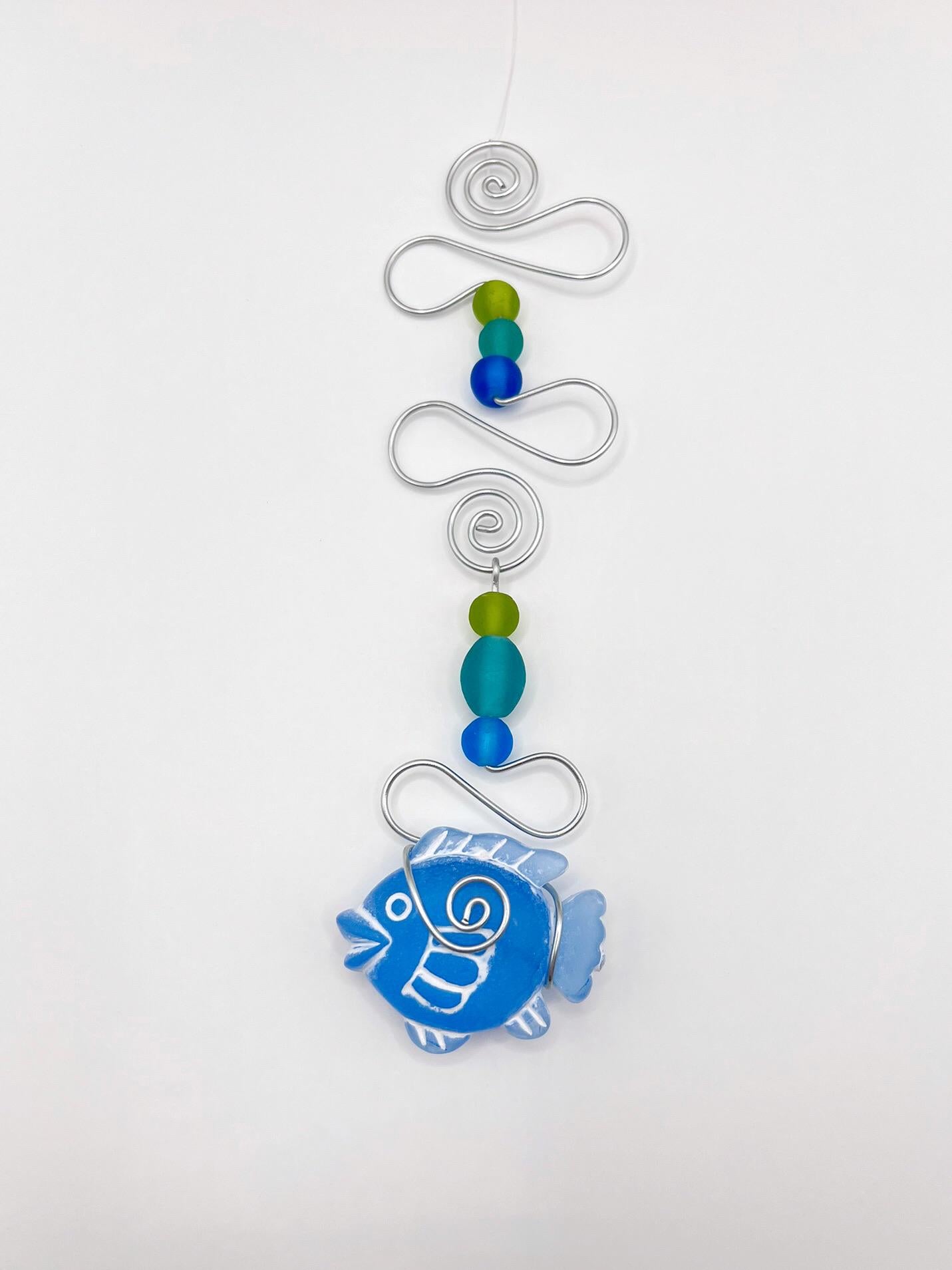 Decorative hanging ornament with blue fish, wire and colourful beads on a white background