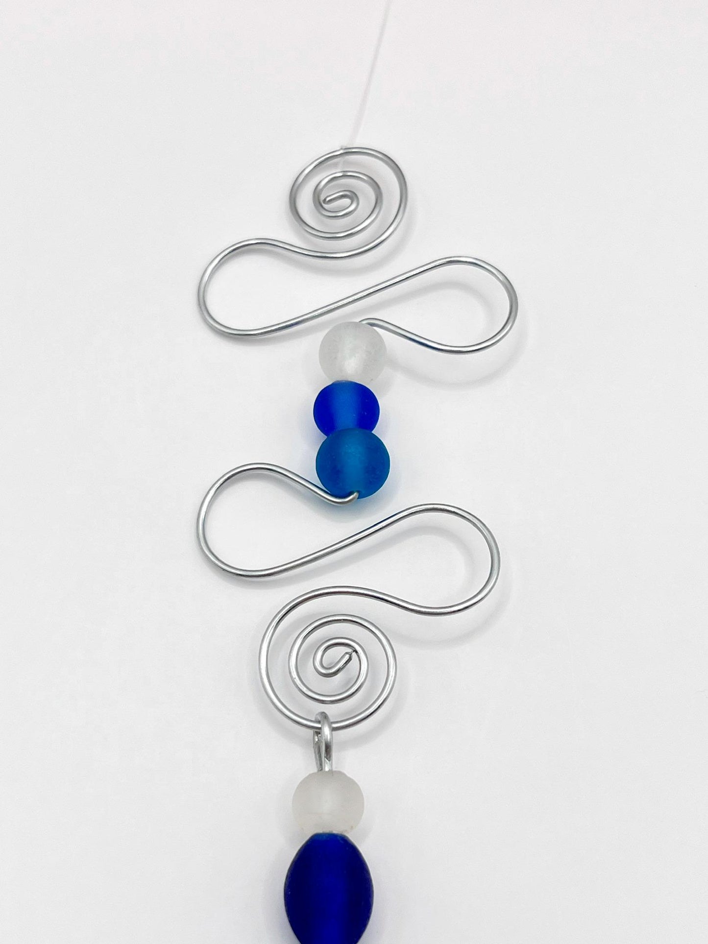 Close up of decorative hanging fish ornament with wire and blue beads on a white background