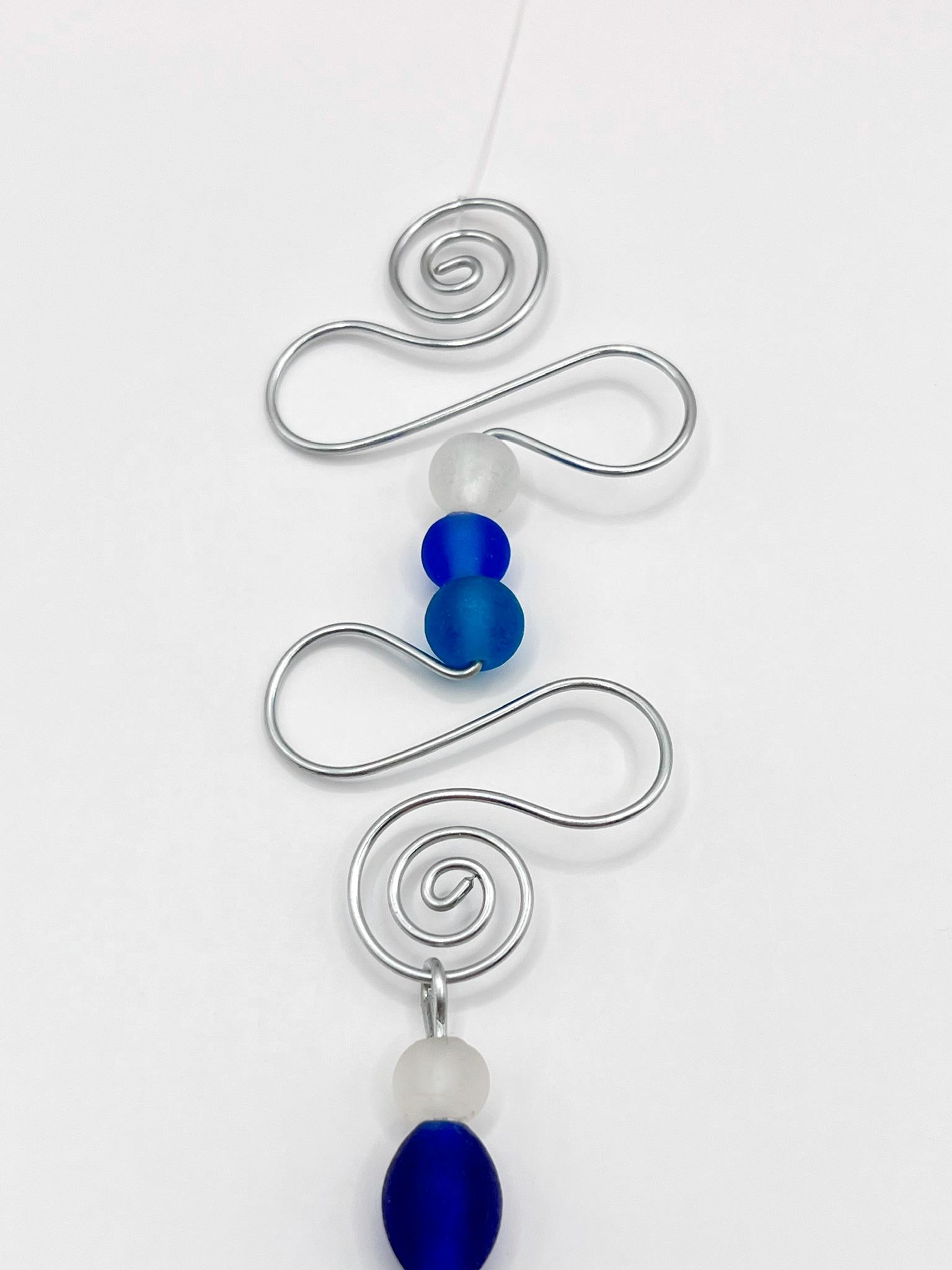 Close up of decorative hanging fish ornament with wire and blue beads on a white background