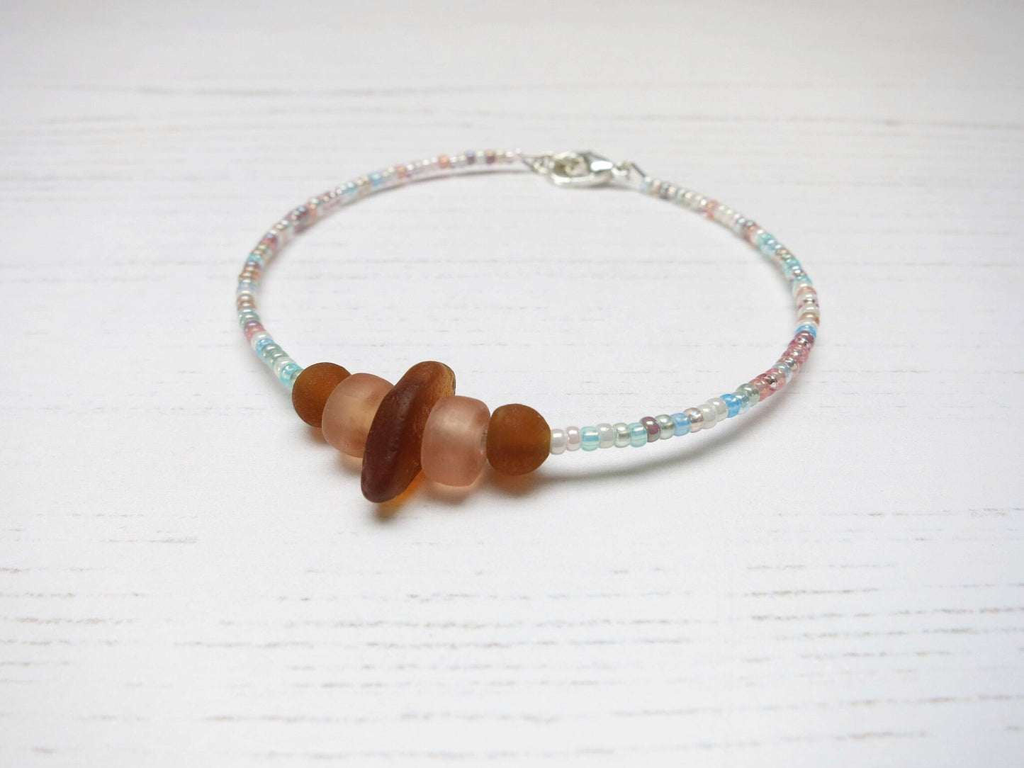 Bracelet with pastel seed beads and burnt orange sea glass laid on a pale background.