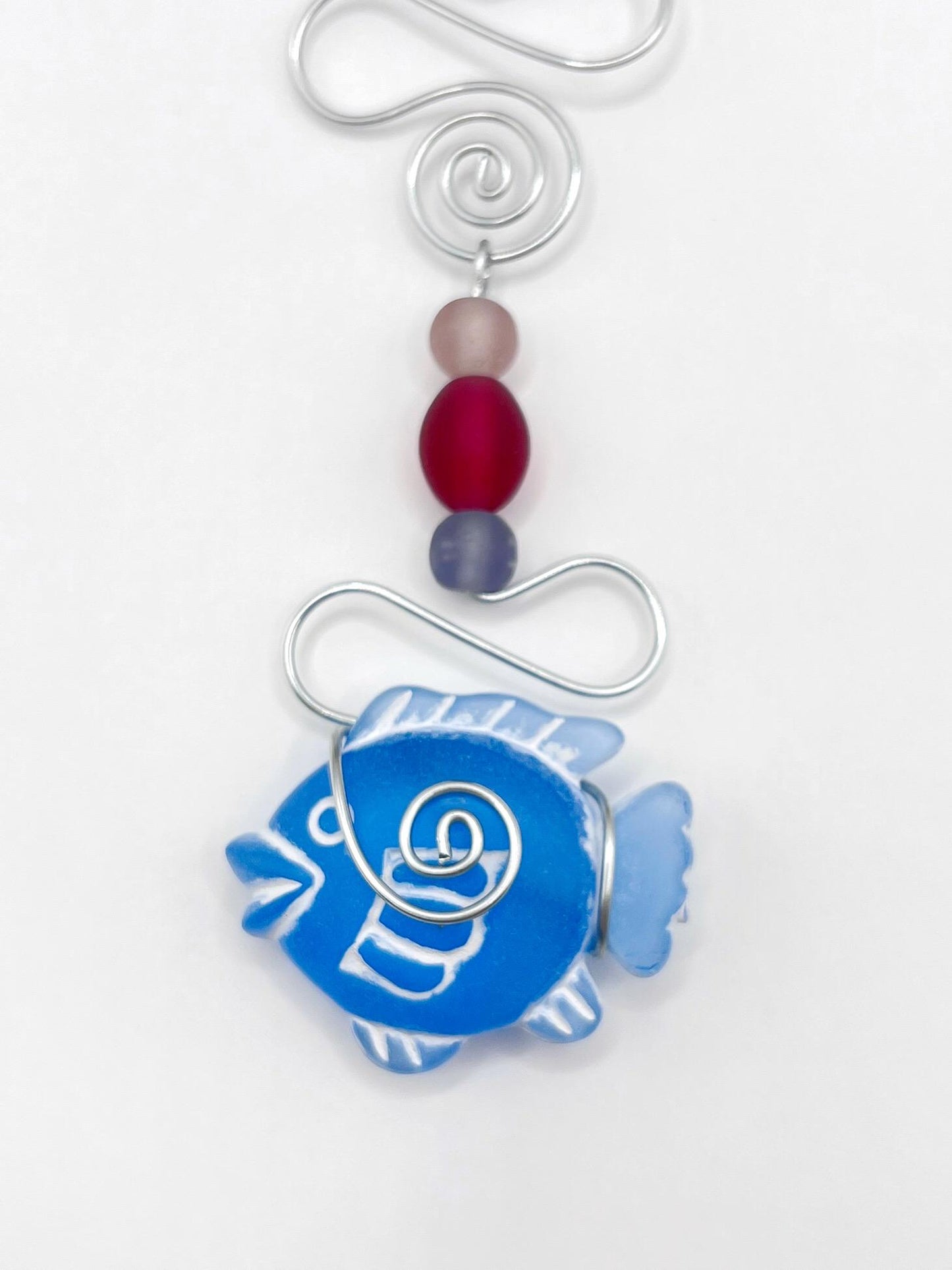Close up of decorative ornament with blue fish, wire and colourful beads on a white background