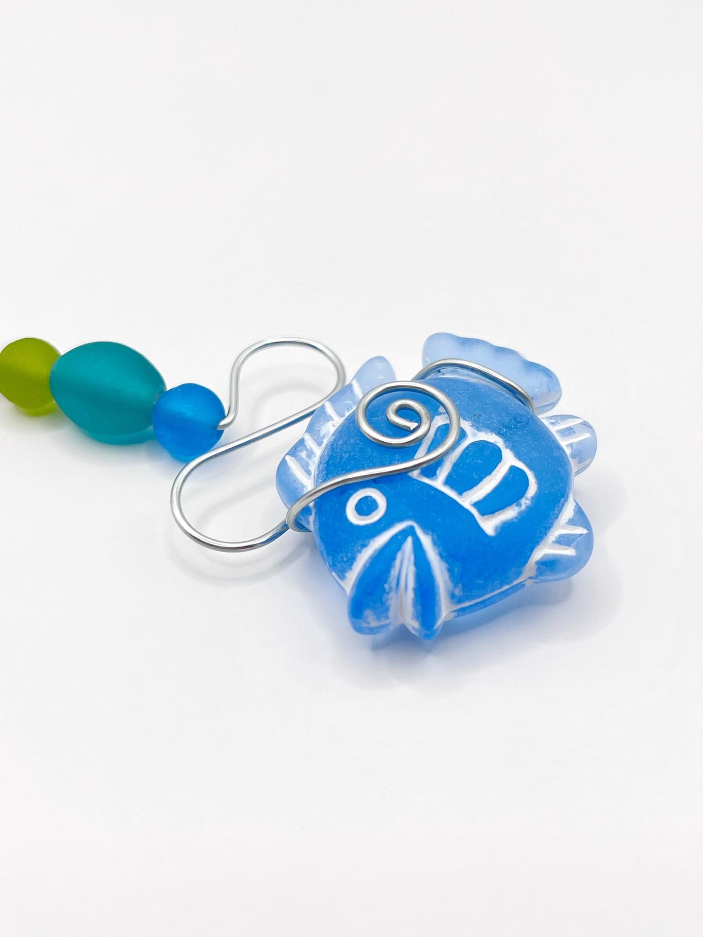 Close up of decorative hanging ornament with blue fish, wire and colourful beads on a white background