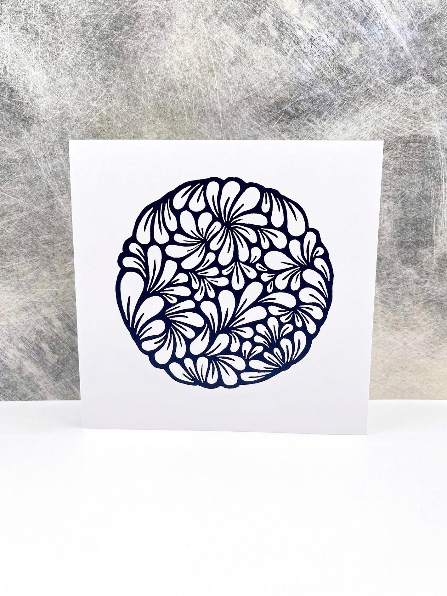 Original navy blue lino printed mussel shell pattern on white card stood against a textured background. 