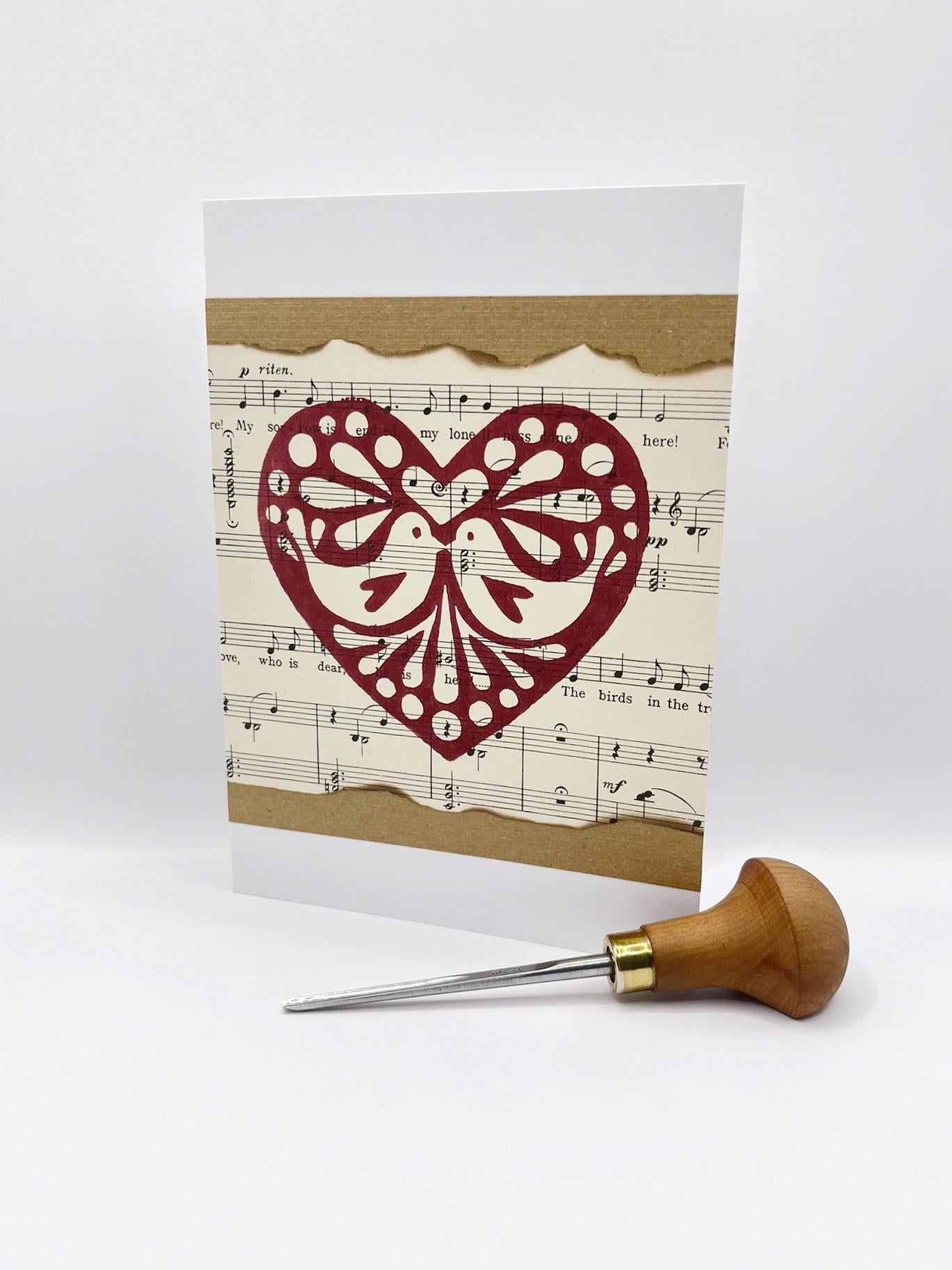 Card with original lino printed heart design on sheet music. Photo includes lino cutting tool used.
