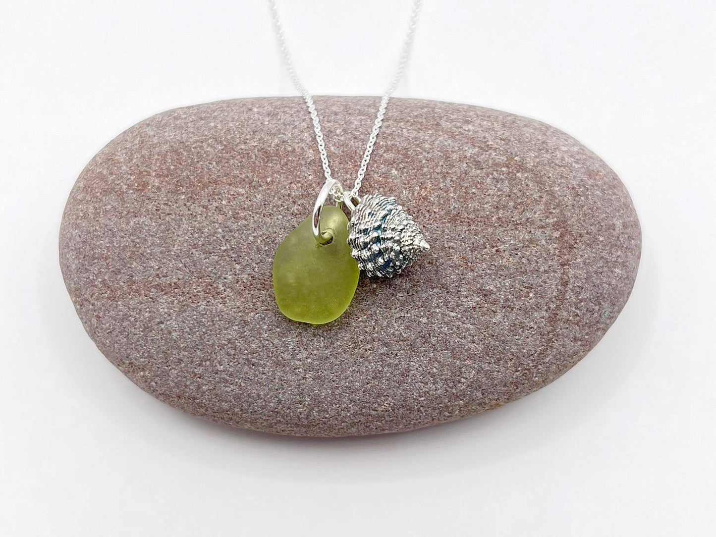 Necklace with lime green sea glass and silver shell charm laid on a purple stone.