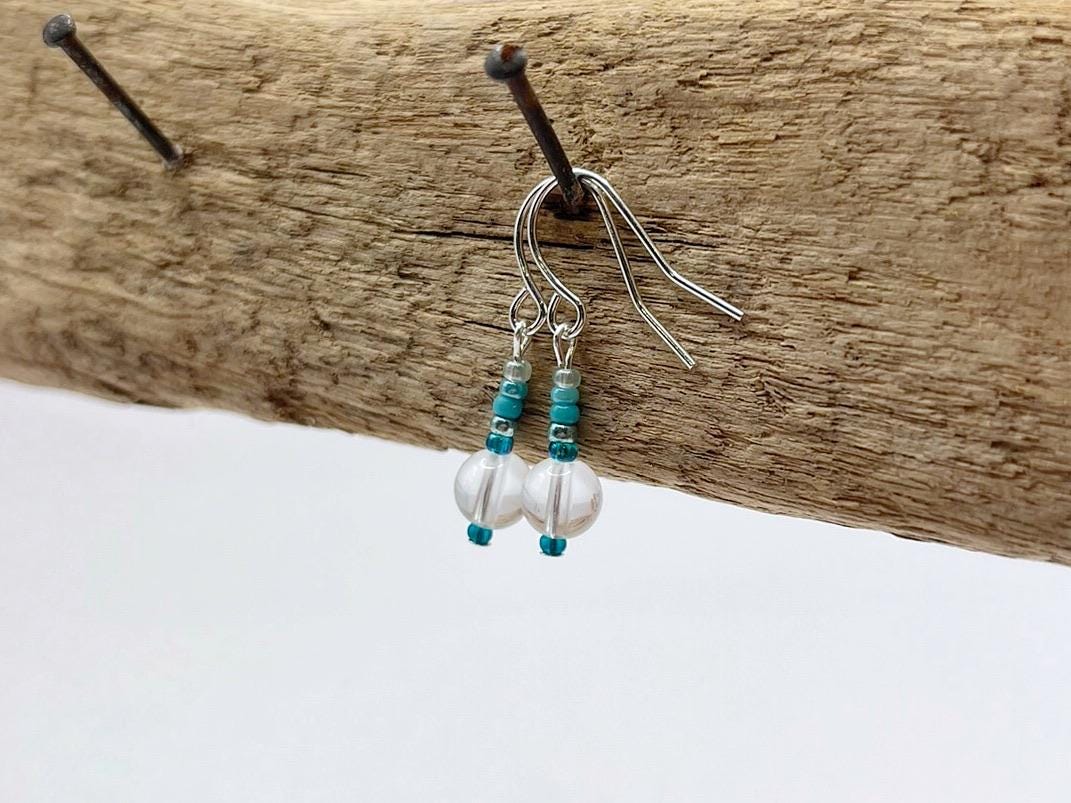 Pair of earrings with clear crystal and turquoise seed beads hanging on driftwood.